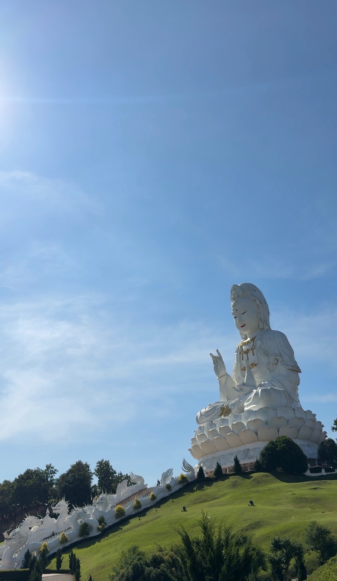 The enormous white Guan Yin statue above the green hillside and dragon-lined staircase at Wat Huay Pla Kang
