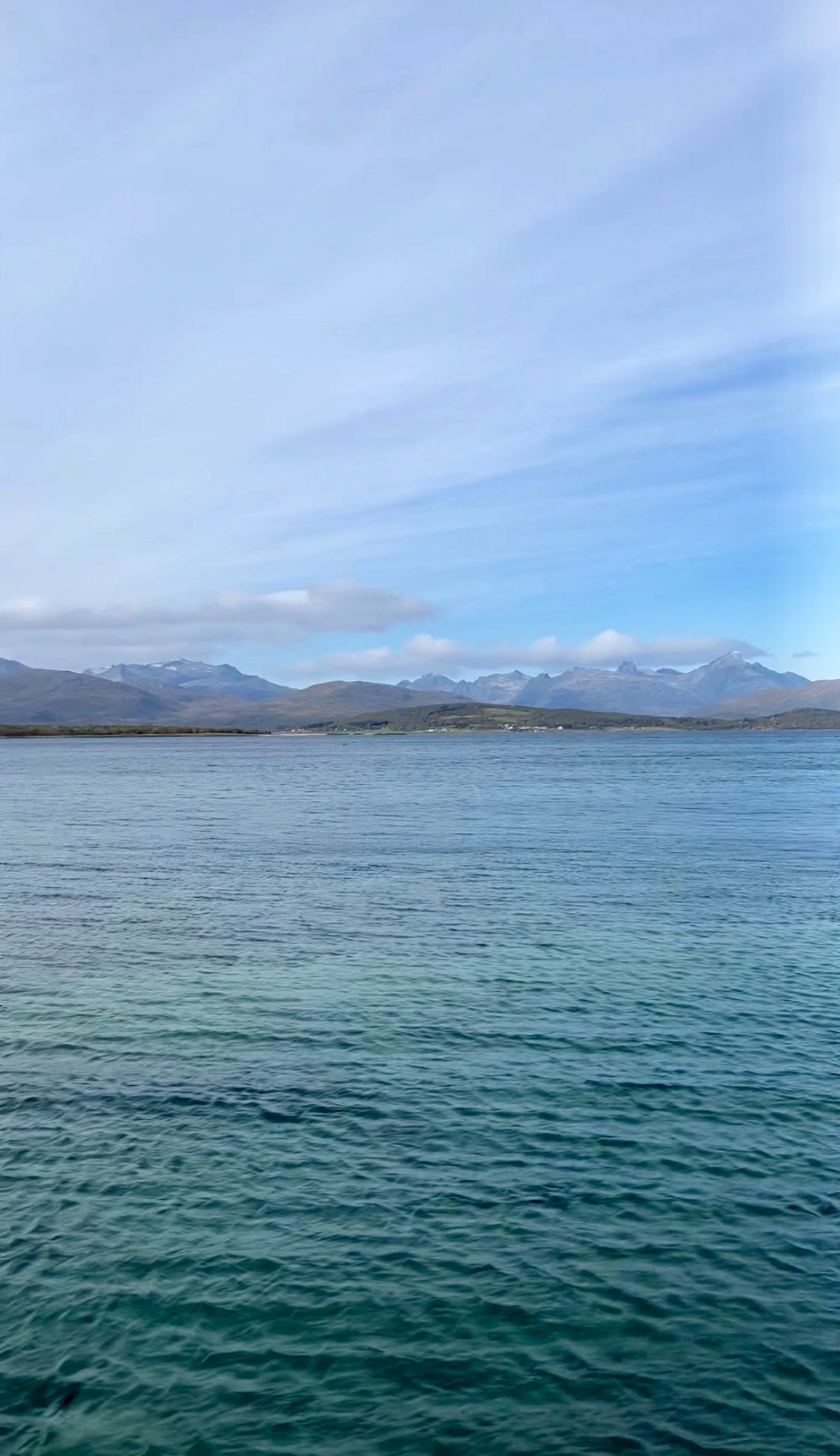 Calm turquoise fjord water near Tromsø, Norway, with snow-dusted Arctic mountain peaks on the far shore.