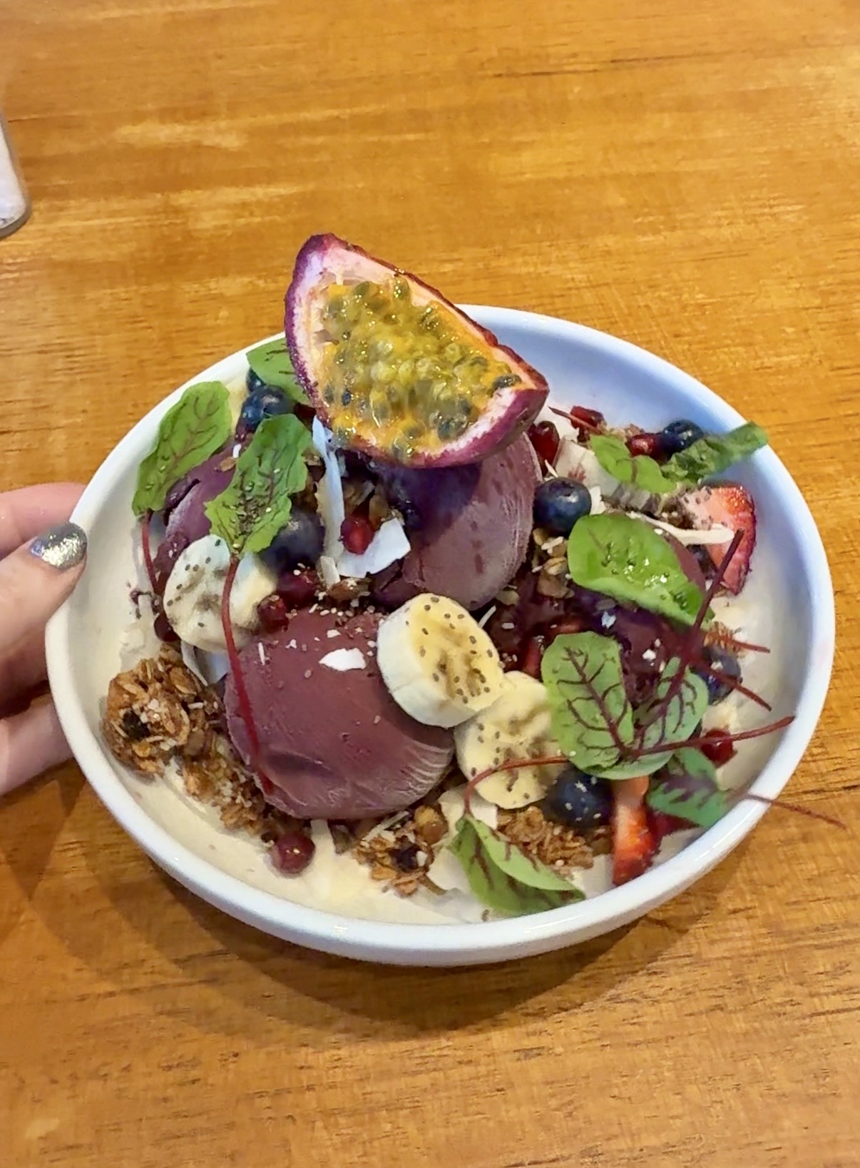A purple berry smoothie bowl topped with banana, granola, blueberries and a passion-fruit half in Sydney
