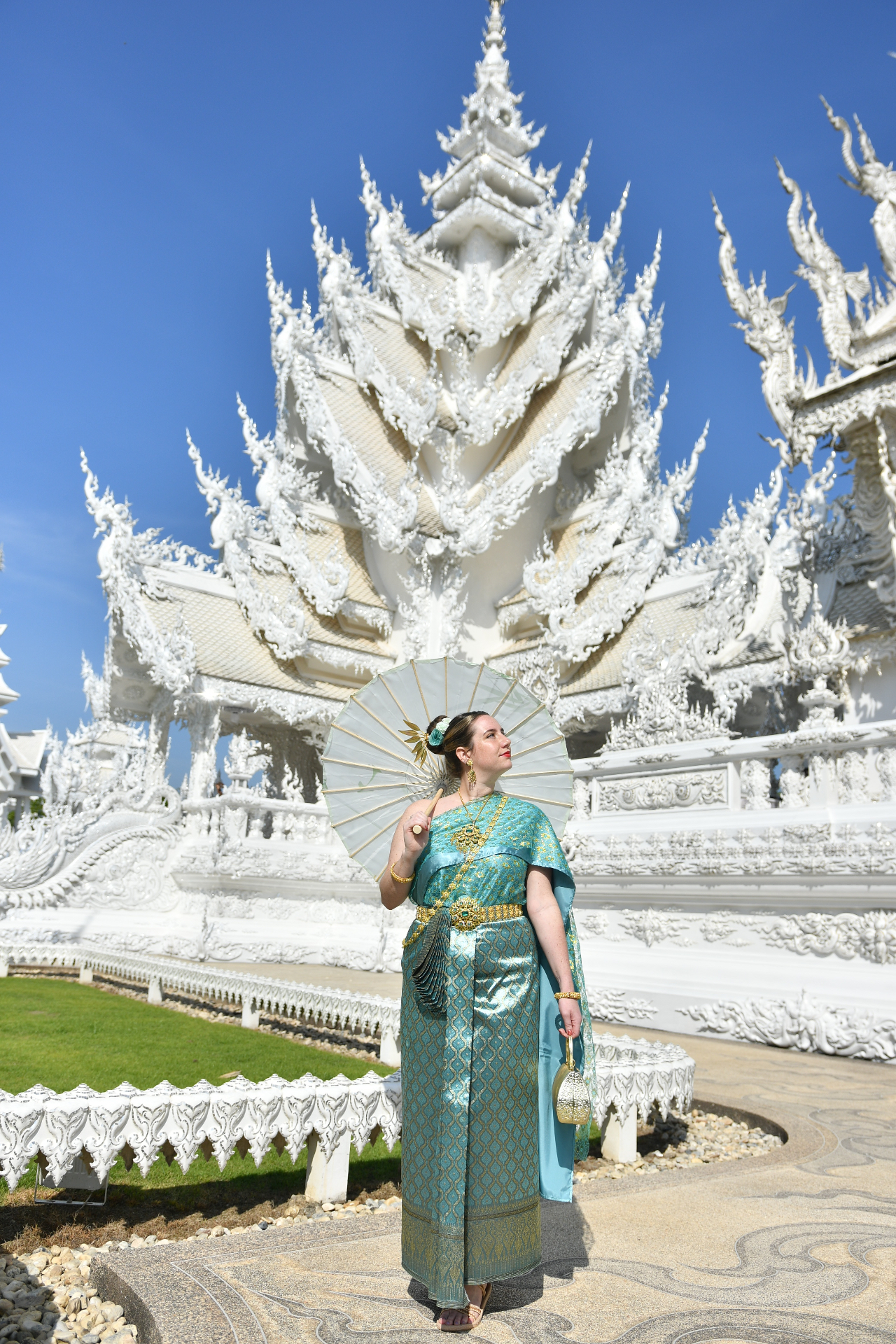 Miranda wearing turquoise and gold traditional Thai clothing and holding a parasol at the White Temple in Chiang Rai