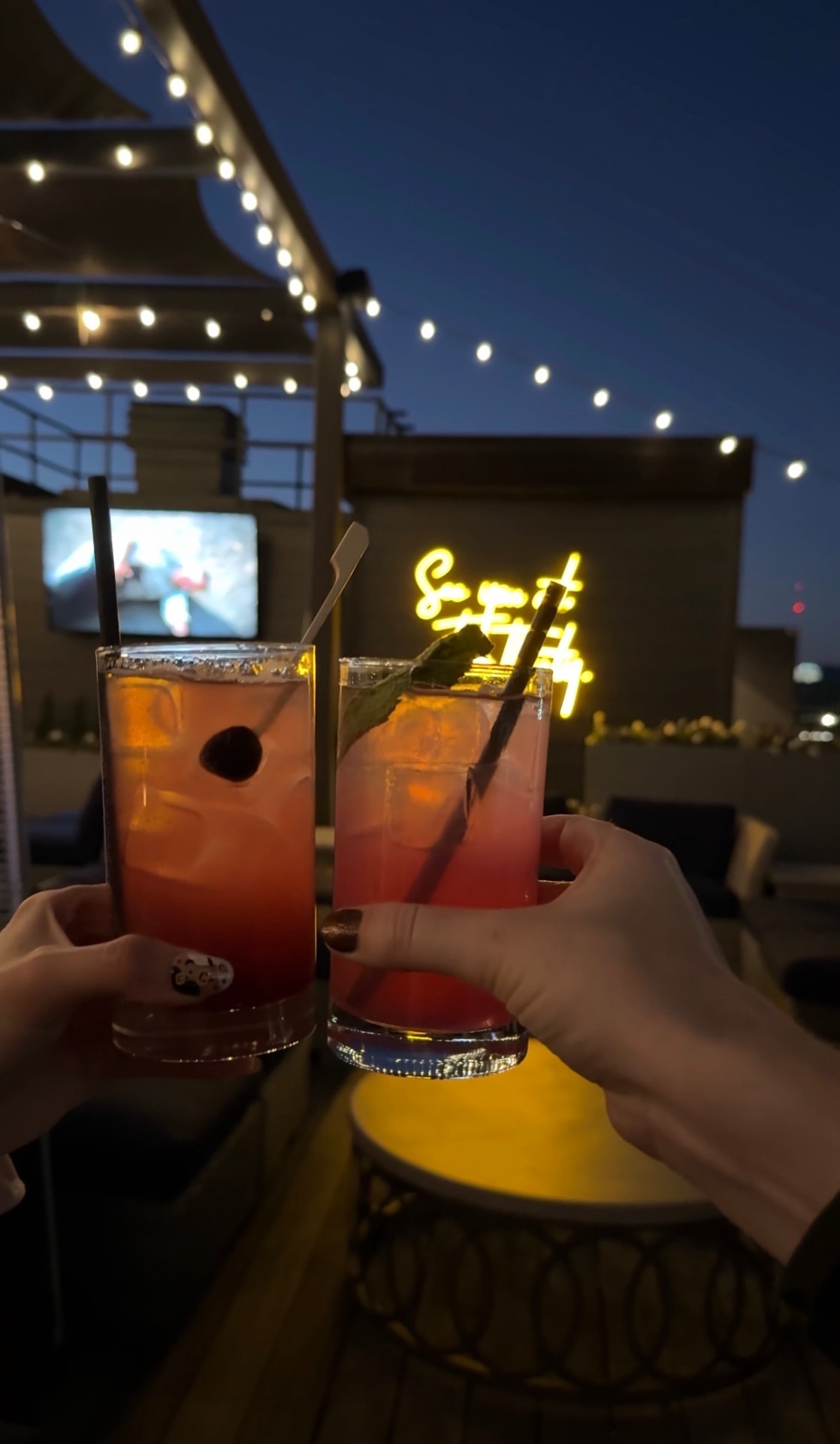 Two cocktails raised in a toast under string lights on the Five Thirty Lounge rooftop in downtown Knoxville at dusk