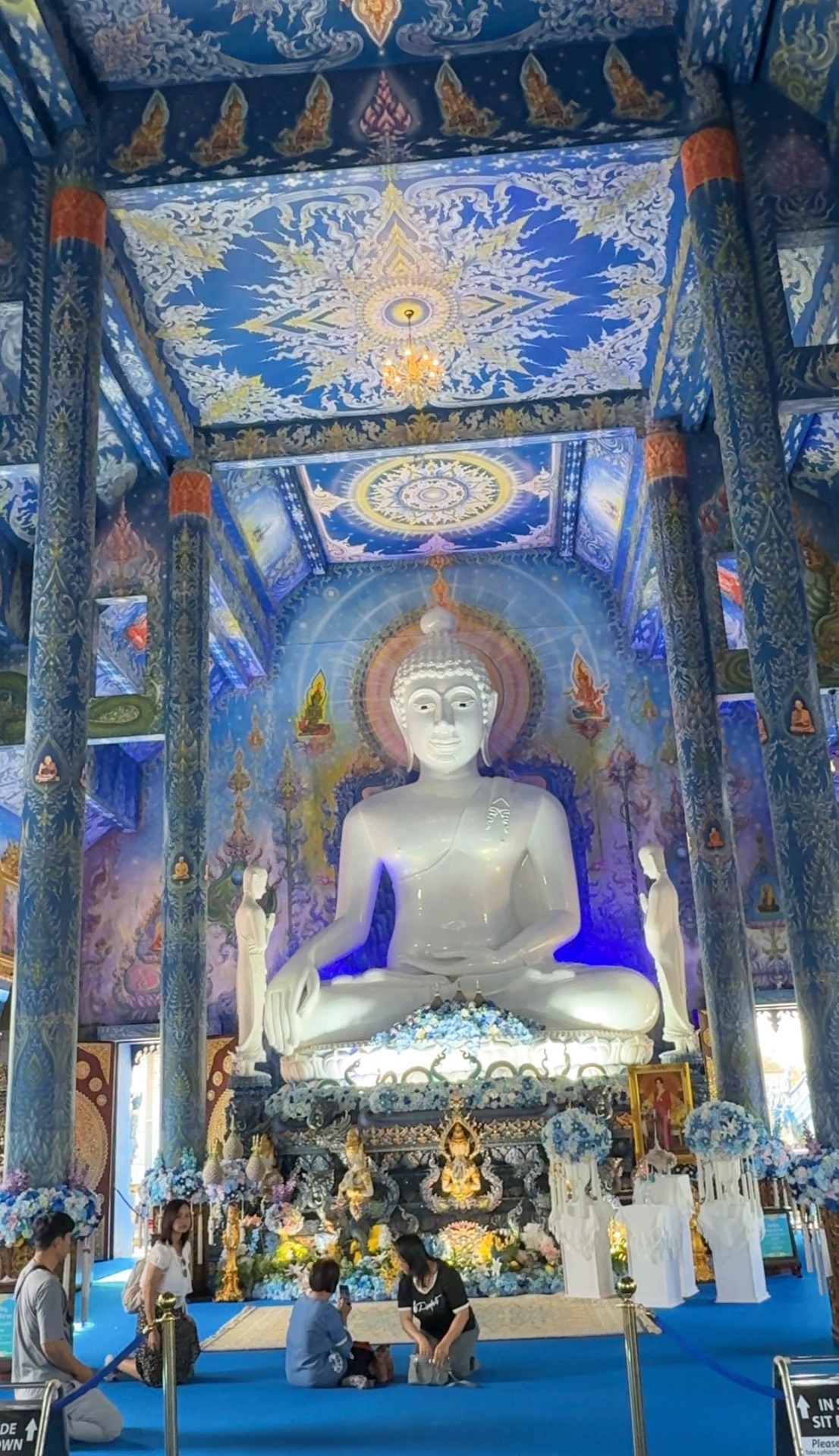 White seated Buddha beneath the intricate blue and gold ceiling of Wat Rong Suea Ten in Chiang Rai