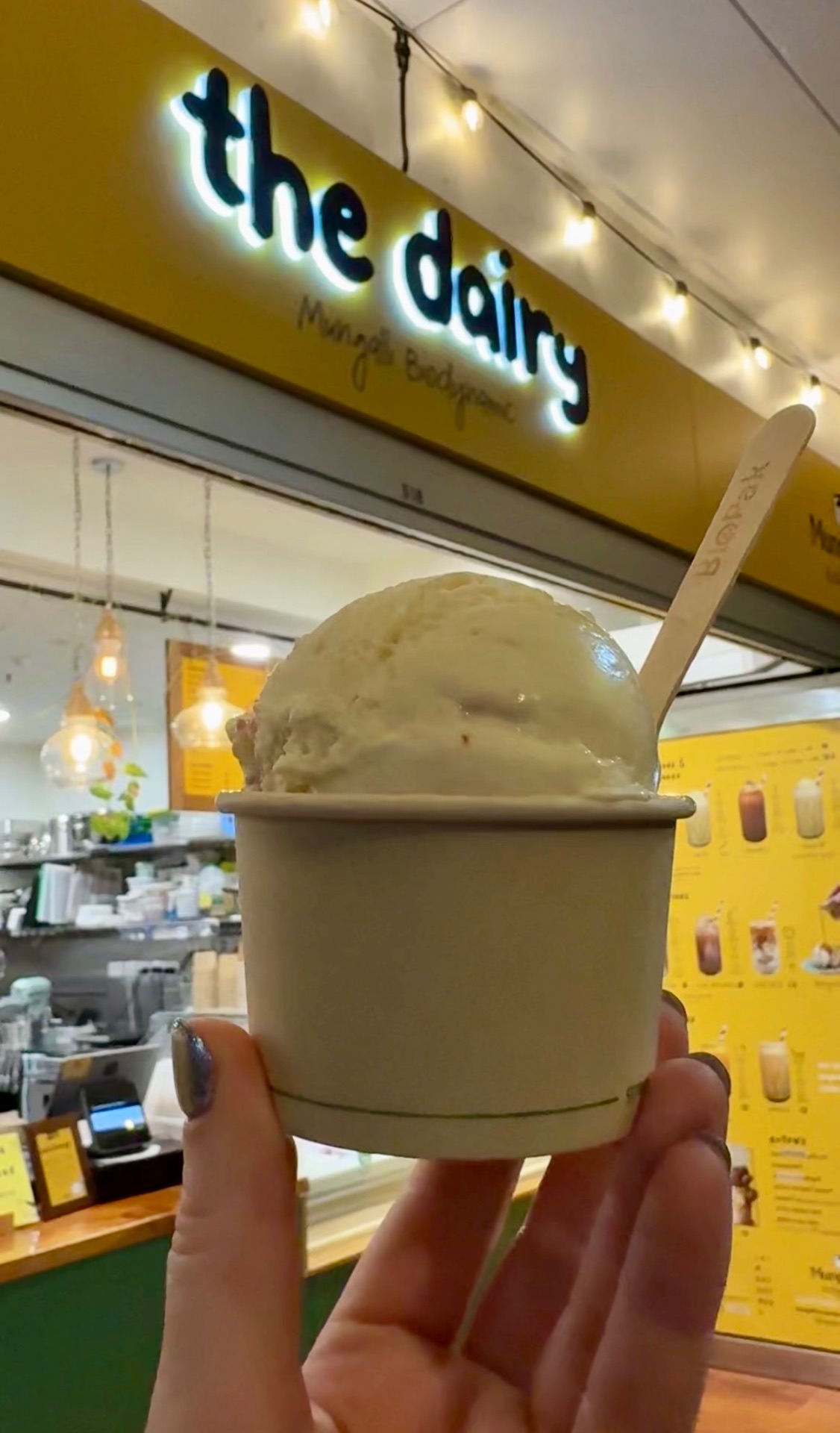 Scoop of ice cream in a cup held up in front of The Dairy sign in Cairns