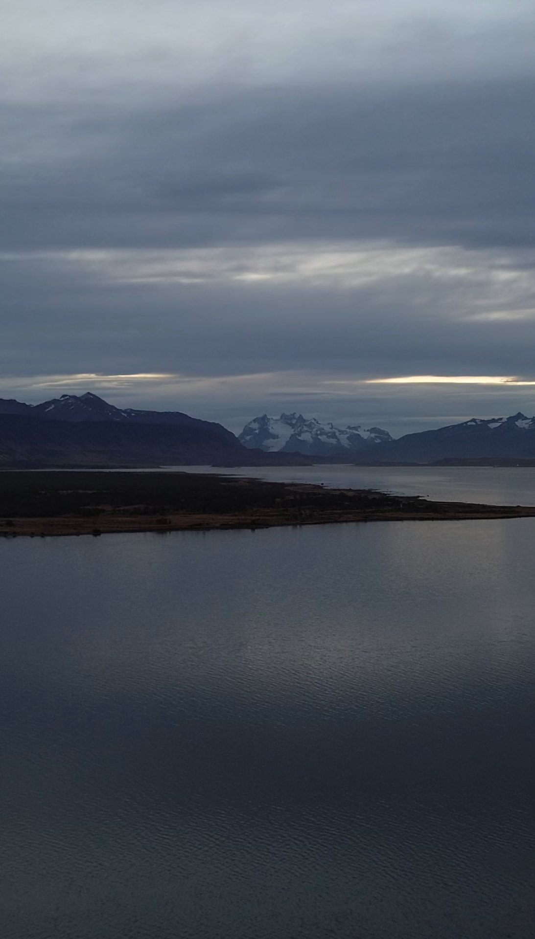 Calm water and snow-dusted mountain peaks under a cloudy sky in Patagonia