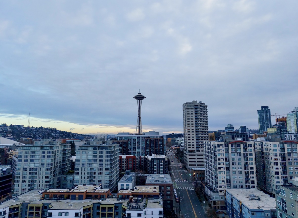 The Seattle skyline at dusk with the Space Needle rising above downtown buildings under a cloudy sky