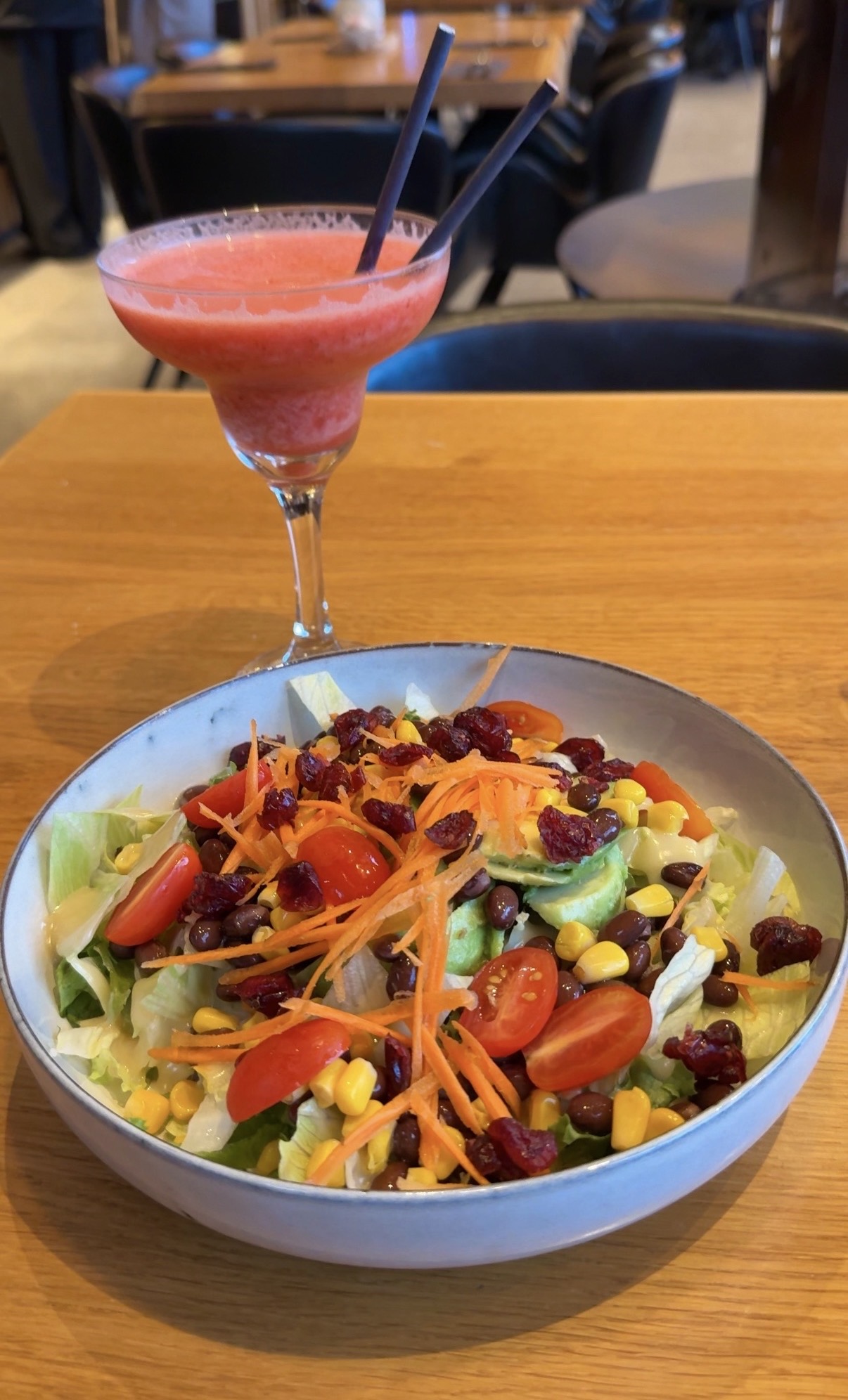 Salad with shredded lettuce, cherry tomatoes, carrots, corn, black beans, avocado and dried cranberries beside a pink blended drink at Forest Lagoon